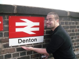Scott at Denton station Scott stands in front of the sign at Denton station entrance